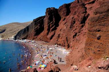 people on beach with red rock walls in the background