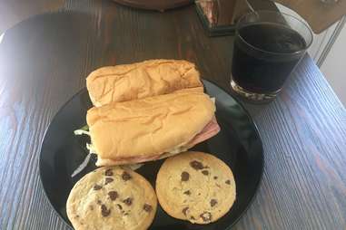 Diet Coke in a glass, two chocolate chip cookies, and two Subway sandwiches on a plate