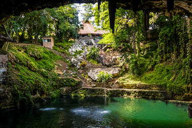 a jungle home and stairway leading down into a natural pool