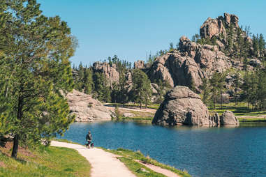 a person walking on a trail next to a lake surrounded by large stacked rocks