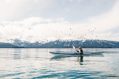 person canoeing in a lake surrounded by snowy mountains