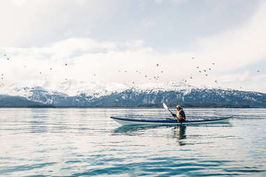 person canoeing in a lake surrounded by snowy mountains