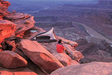 a person camping on a cliff above a rocky river canyon