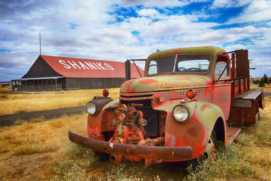 a rusting red truck in front of a farmhouse