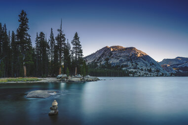 a lake lined by pine trees with mountains in the distance
