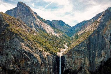 a waterfall dropping down off of a forested cliff