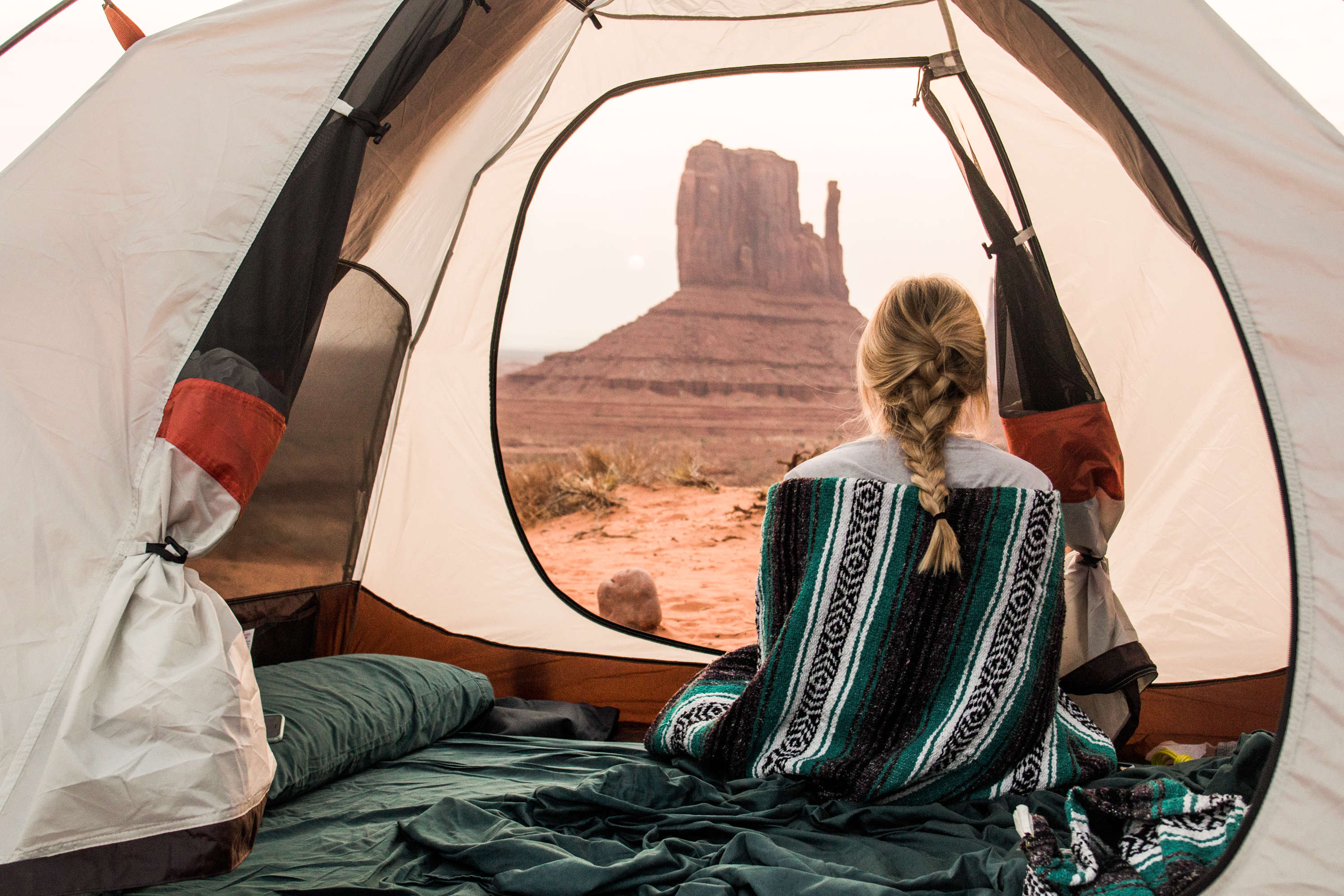 blanket-wrapped woman in a tent staring out at the desert
