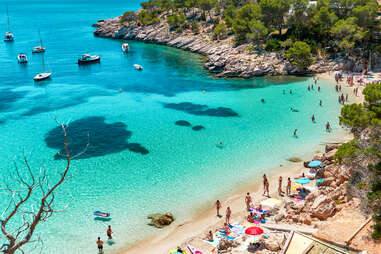 people lounging and boats near a beautiful beach in Ibiza, Spain