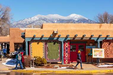 people in an adobe town beneath a large mountain