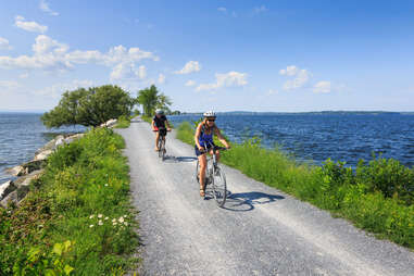 people biking along a greenery-lined road in the middle of a lake