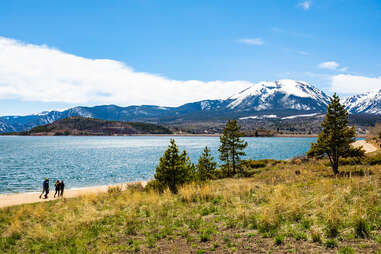 people walking along the shore of dillon lake reservoir with mountains in background