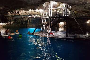 a ladder and platform in an underground natural pool filled with swimmers