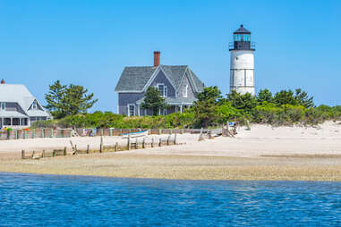 Sandy Neck Lighthouse dotting the blue coast of Cape Cod Bay along a sandy beach.