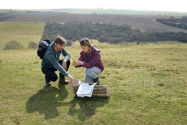 couple at the top of a hill looking through a geocache's contents