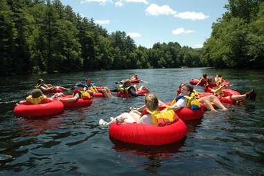 people in inner tubes floating down a tree lined river