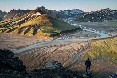 man standing at the base of a river and mountain