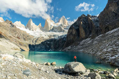 Man with hiking poles and red t-shirt standing on a rock admiring Laguna Sucia and Fitz Roy range from above in autumn