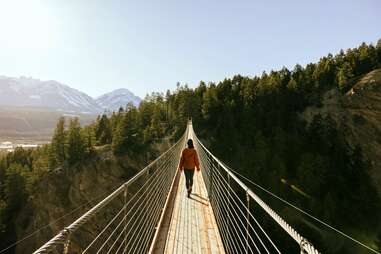 woman walking across long skybridge toward forest and mountains in Canada