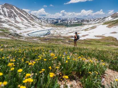 woman hiking through wildflowers in a mountain range