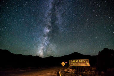 Information Sign On Road By Silhouette Mountains Against Star Field