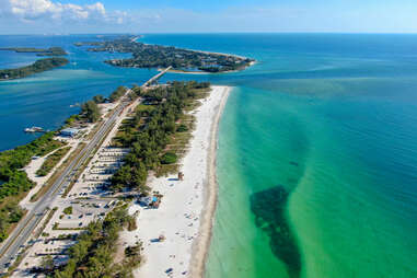 Aerial view of Coquina Beach with white sand beach, trees, and the main road