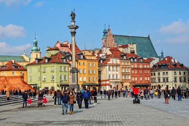 People walk in Castle Square in Warsaw in Old Town with the Column of King Zygmunt III Waza & ancient houses in the background