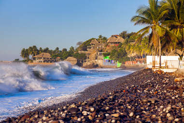 waves crashing against a rocky shore near a tropical village