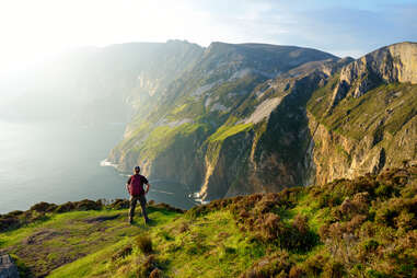 person standing looking out at the ocean from enormous cliffs