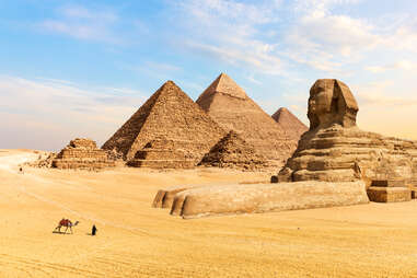 person guiding a camel through the sands by the Great Pyramids and the Sphinx