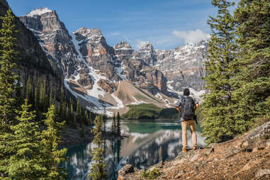 man standing on a hill overlooking a lake surrounded by mountains and trees