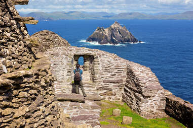 Back view of woman pausing to take pictures through arch in ruins of Skellig Michael monasteries, County Kerry, Ireland