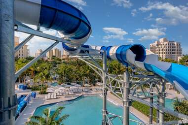a water slide winding past a hotel, pool, and palm trees