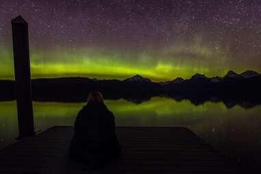 a person looking out at the northern lights above mountains