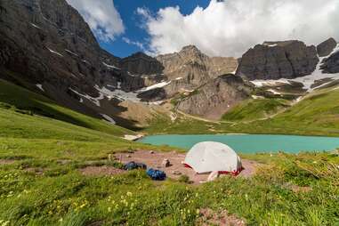 A tent set up in front of a blue-green lake and towering snowy mountains.