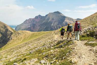 Three hikers on a trail facing large mountains in the distance