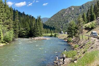 people fishing by a river's edge surrounded by forested mountains