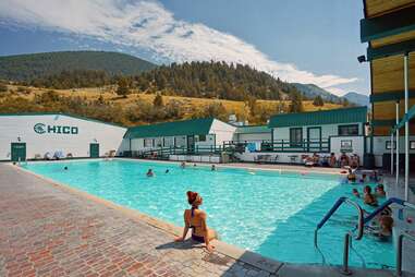 a woman sitting at the edge of a hot spring pool surrounded by mountains