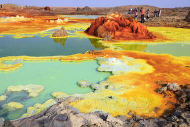 people walking around colorful acid pools surrounded by rock in the desert