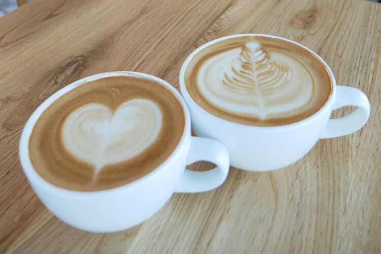 Close up white coffee cup with heart shape latte art on wood table at cafe  - Shamrock Foods