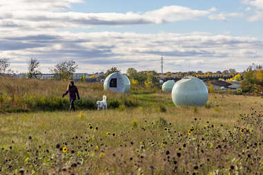 a woman walking through a field in jarry park with dome art 