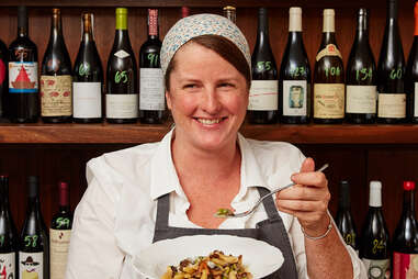 a woman holding a bowl of food in front of a wine shelf