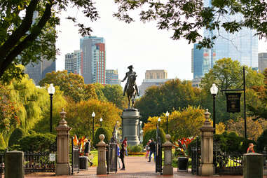 people walking past a statue in a public garden