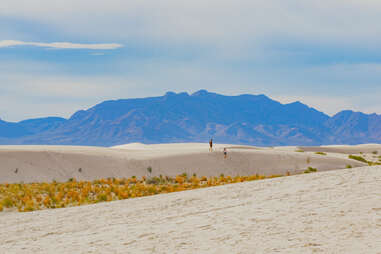 people walking across sand dunes surrounded by mountains