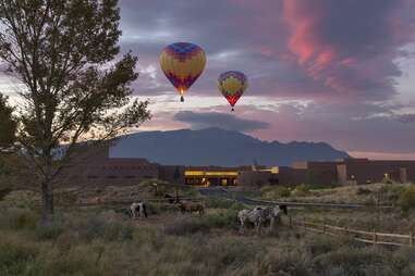 hot air balloons above horses and an adobe ranch
