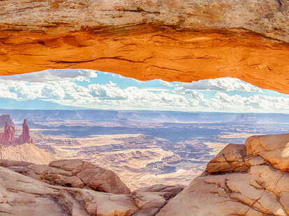 Panoramic view of famous Mesa Arch, iconic symbol of the American West, illuminated golden in beautiful morning light on a sunny day with blue sky and clouds, Canyonlands National Park, Utah, USA