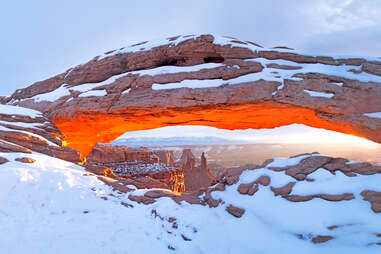 enormous stone mesa arch covered in snow in canyonlands national park