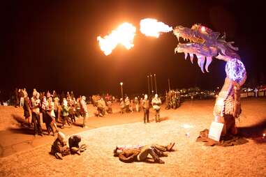 people laying below a dragon ice sculpture blowing fire