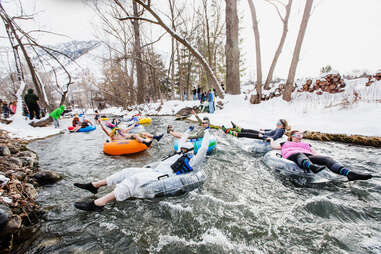 people tubing down an icy river surrounded by snowy banks