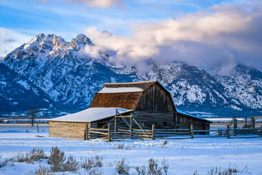 a wooden barn with enormous wintry mountains in the distance
