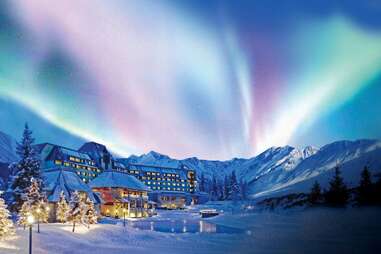 the northern lights dancing above a large snow covered alaskan resort